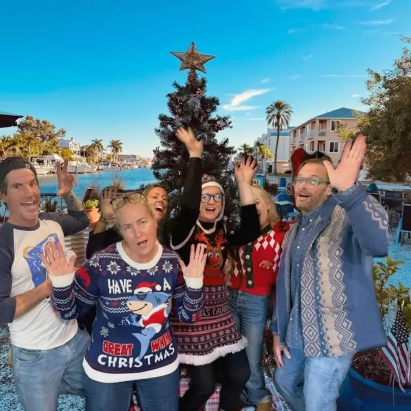 Guests in holiday sweaters by the Christmas tree on the patio