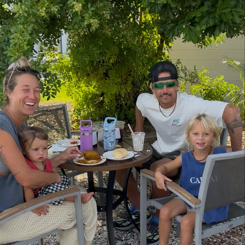 A family at a patio table under the trees