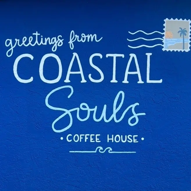 A painted "greetings from Coastal Souls Coffee House" sign on a blue wall