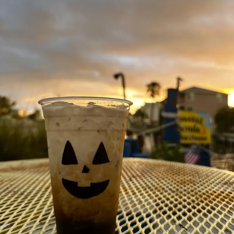 An iced coffee with a jack-o’-lantern face, morning sky behind it